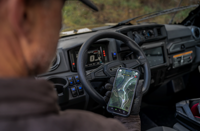 Person standing using RIDEOLOGY THE APP POWERSPORTS in front of their side by side.