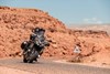 Front angle of people riding a motorcycle on a desert highway.