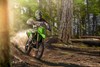Three-quarter front angle of a person riding a motorcycle off-road through trees.