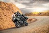Three-quarter front angle of people riding a motorcycle over a desert highway.
