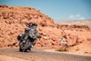 Front angle of people riding a motorcycle on a desert highway.