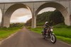 Profile angle of person riding a motorcycle on a in front of a bridge.