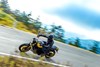 Side angle of a person riding a motorcycle on a highway in the forest.