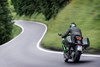 Three-quarter rear angle of a person riding a motorcycle on a paved road.