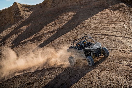 Three-quarter front angle of two people riding in a side x side off-road. opens in a new window