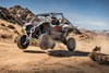 Three-quarter front angle of a person driving a side x side off-road in a desert.