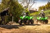 Side angle of two people riding ATVs on a closed course with parental supervision.