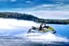 Side angle of a person on a personal watercraft on the water by mountains.