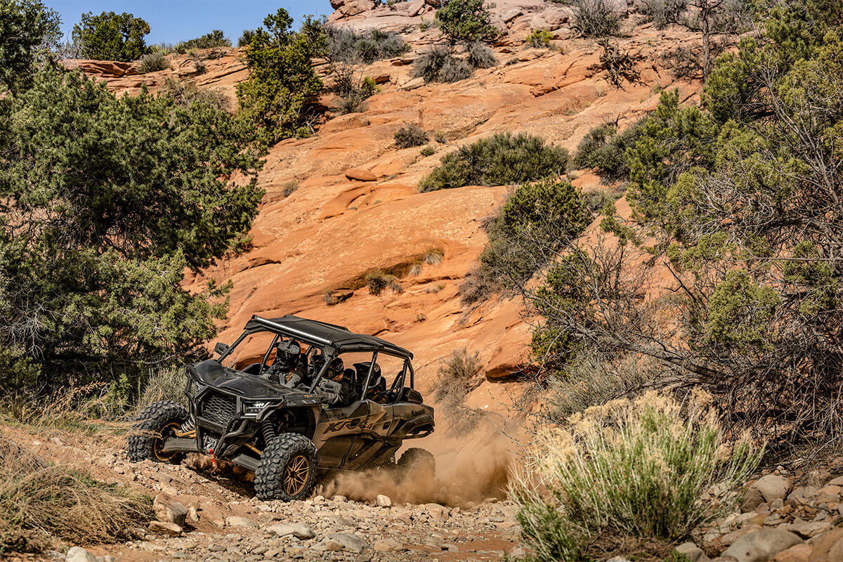 Three-quarter front angle of a person driving a side x side near a rocky hill.