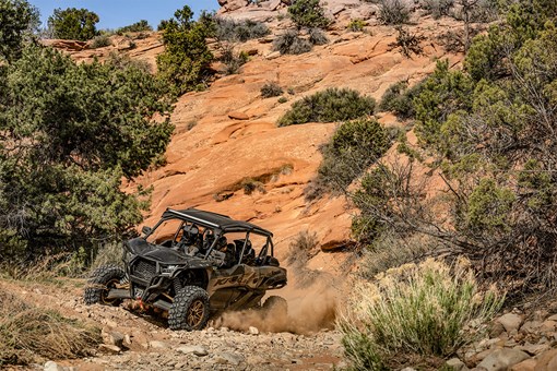 Three-quarter front angle of a person driving a side x side near a rocky hill. opens in a new window