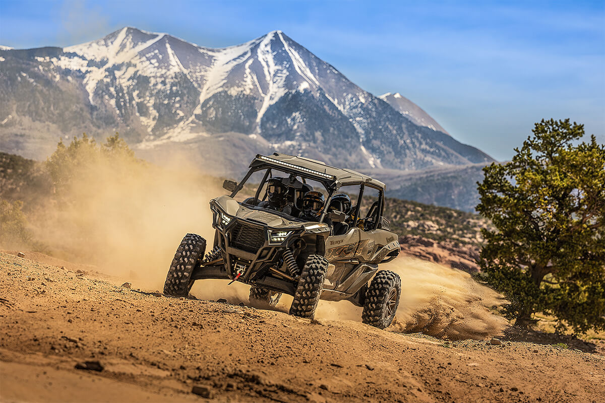 Three-quarter front angle of a person driving a side x side off-road with a mountain in the background.