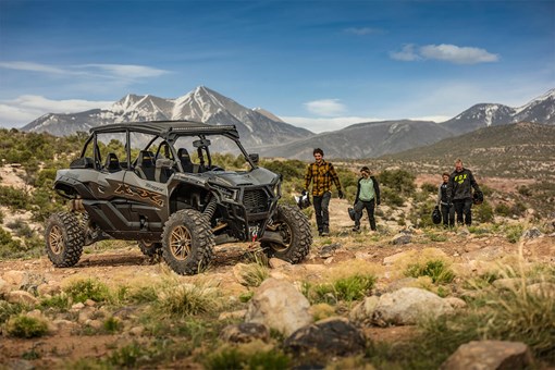 Three-quarter front angle of four people walking towards an idle side x side off-road. opens in a new window