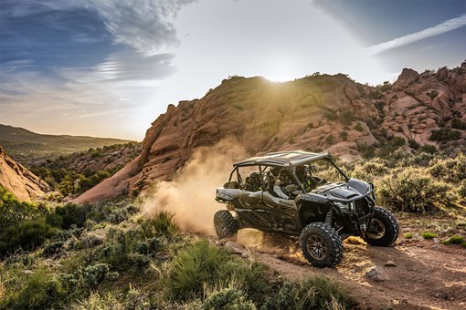 Three-quarter front angle of a person driving a side x side on a dirt trail. opens in a new window