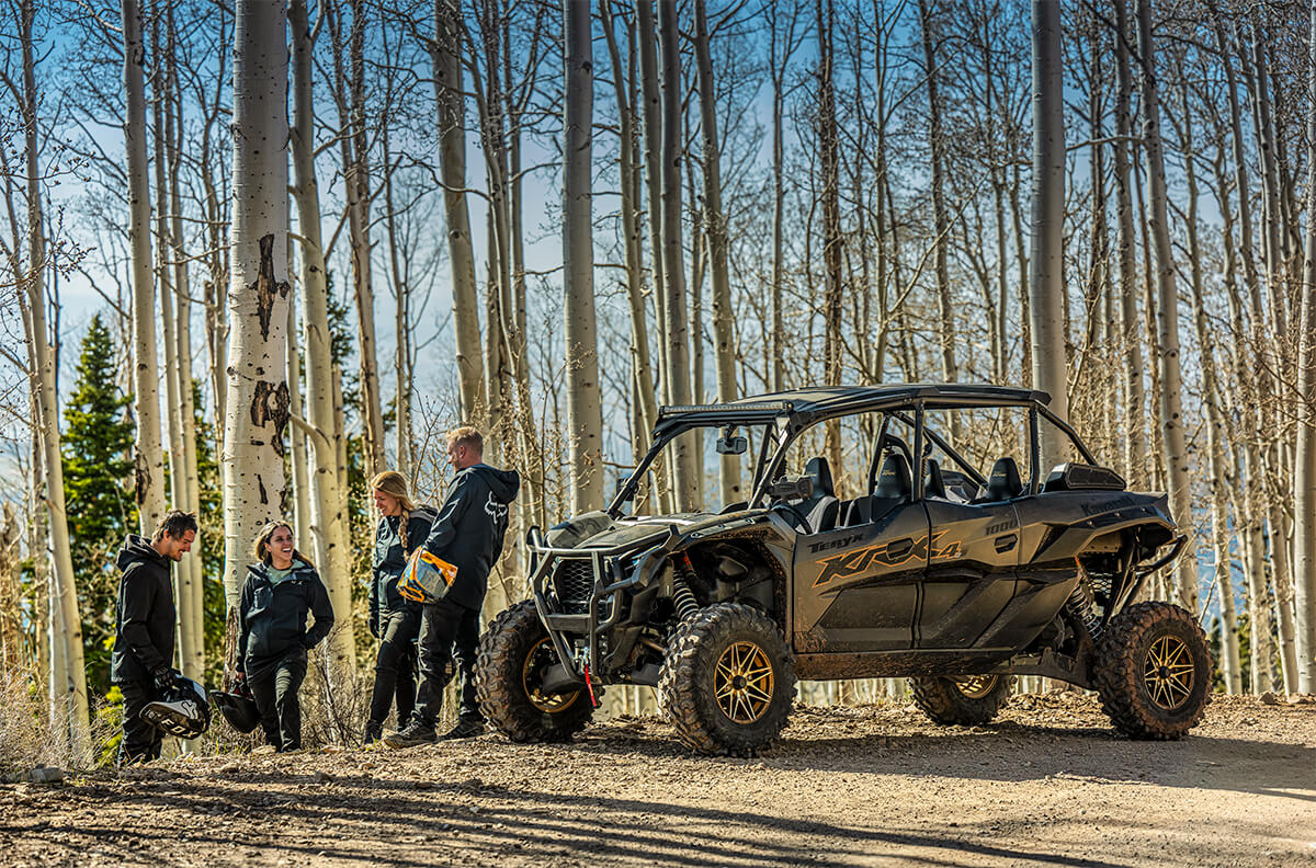 Three-quarter front angle of four people standing next to a side x side off-road.