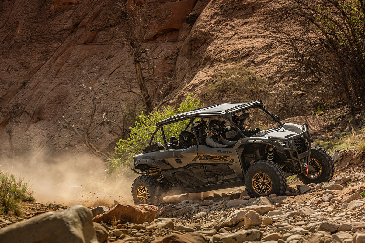 Three-quarter front angle of a person driving a side x side on rugged terrain.