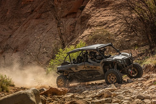 Three-quarter front angle of a person driving a side x side on rugged terrain. opens in a new window