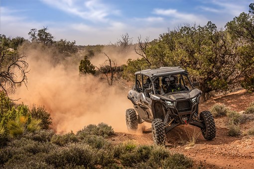 Three-quarter front angle of a person driving a side x side off-road while leaving a trail of dust. opens in a new window