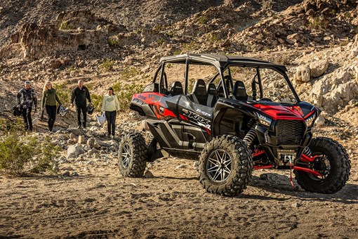 Three-quarter front angle of four people walking towards a side x side off-road. opens in a new window