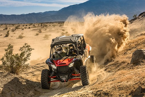 Three-quarter front angle of a person driving a side x side off-road leaving a trail of dust. opens in a new window
