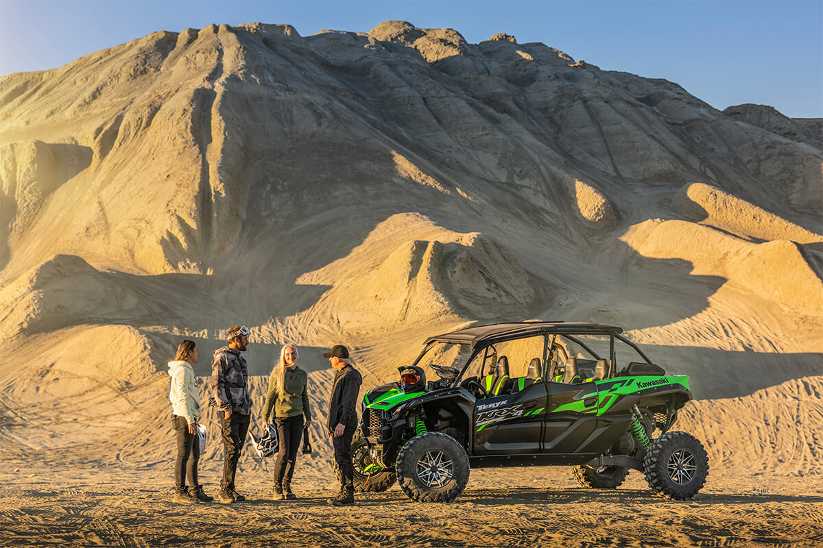 Side angle of four people standing next to a side x side off-road.