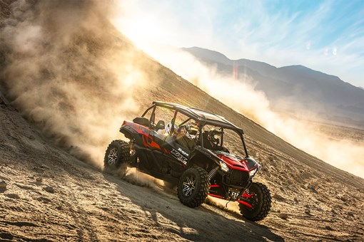 Three-quarter front angle of a person driving a side x side down a dirt hill. opens in a new window