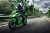 Three-quarter front angle of a person riding a green motorcycle on a highway.