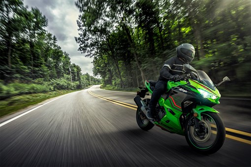 Three-quarter front angle of a person riding a motorcycle down a highway surrounded by trees. opens in a new window