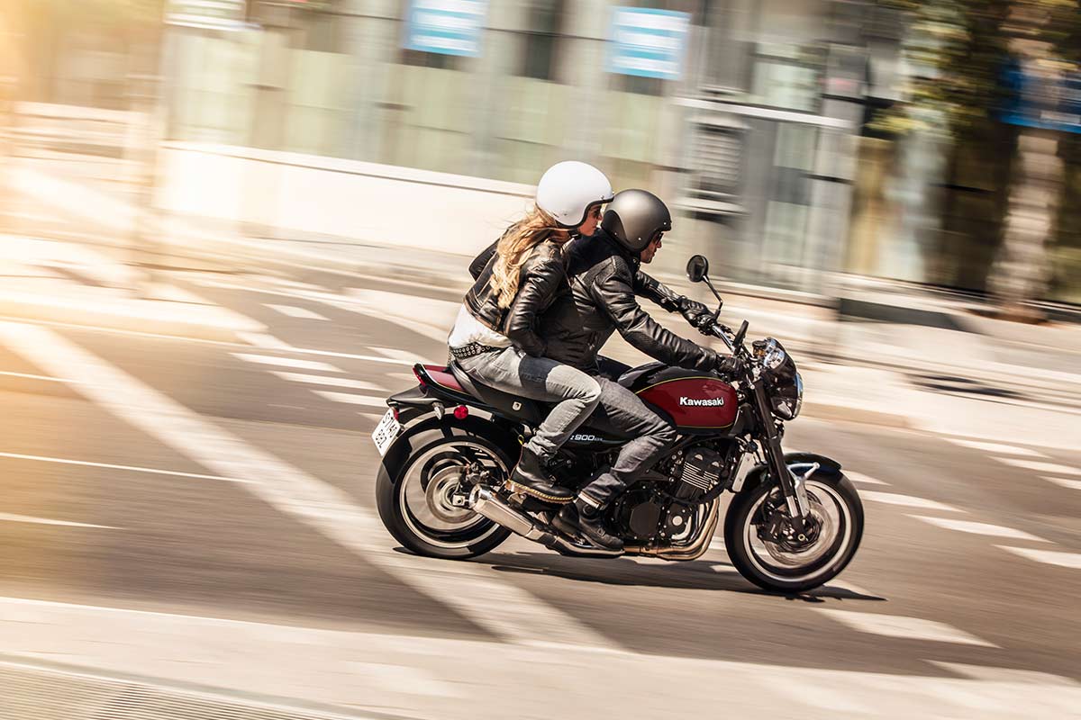 Side angle of two people riding a motorcycle on a paved road.