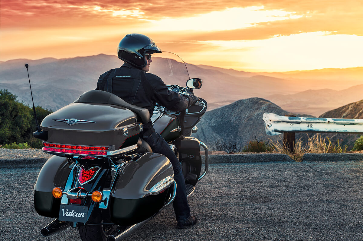 Rear angle of a person sitting on a motorcycle at sunset.