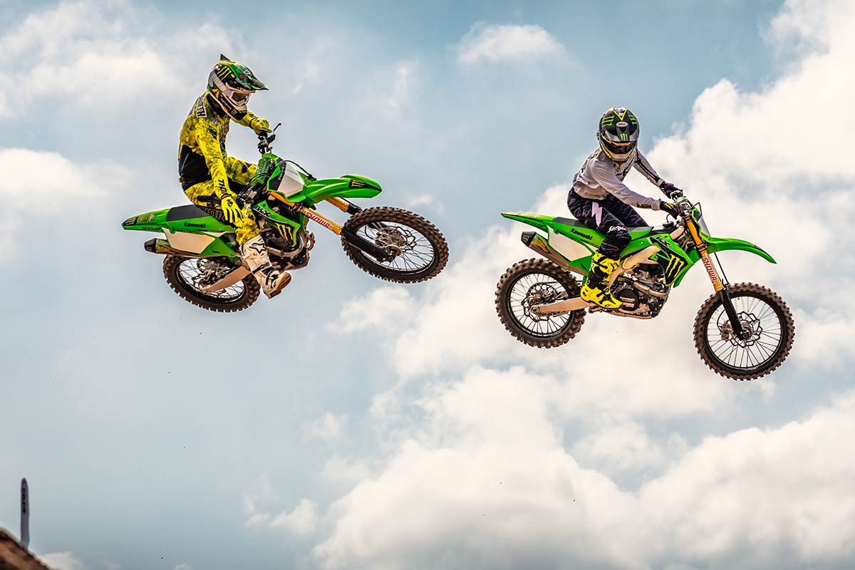 Three-quarter front angle of two people making a jump on a dirt track.