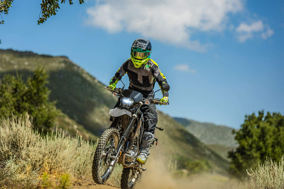 Three-quarter front angle of a person doing a wheelie on a motorcycle off-road.