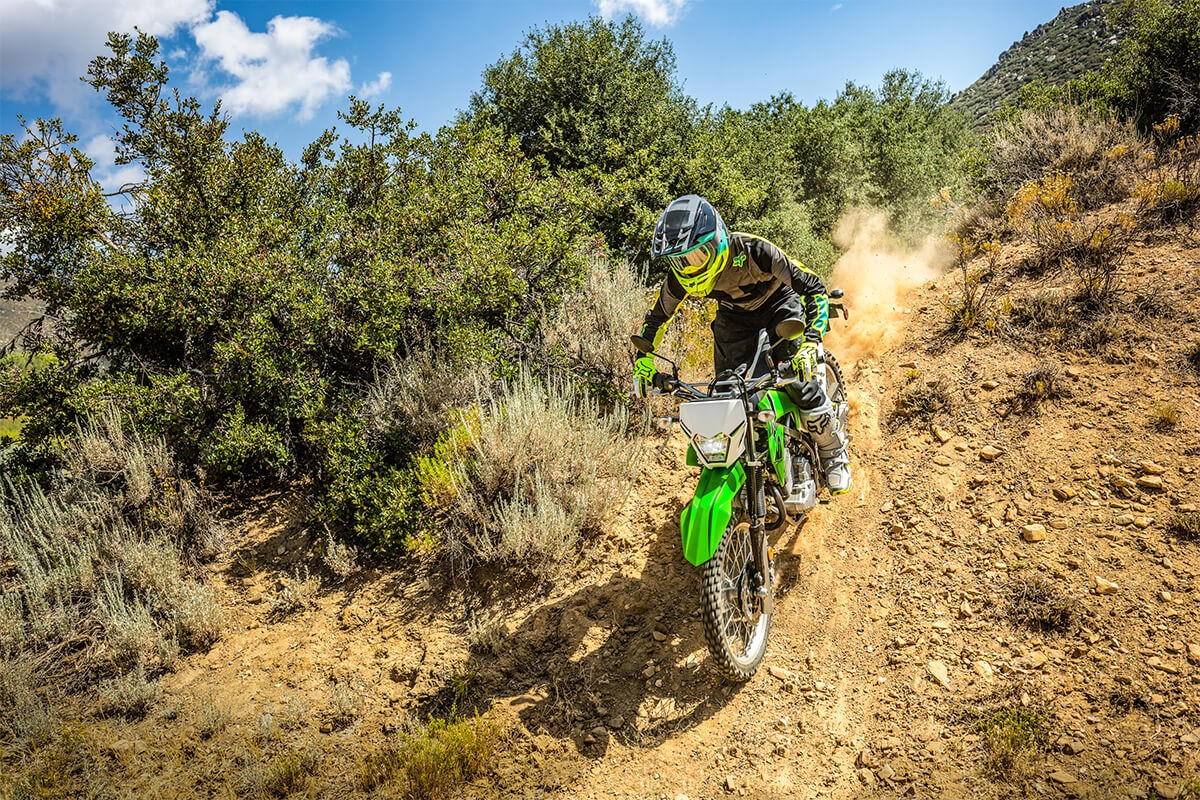 Three-quarter front angle of a person riding a motorcycle down a dirt trail off-road.