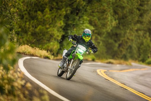 Three-quarter front angle of a person riding a green motorcycle on a highway. opens in a new window