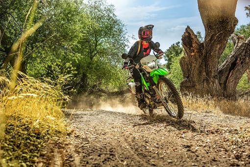 Three-quarter front angle of a person riding a motorcycle on a dirt trail off-road. opens in a new window