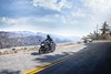 Three-quarter front angle of a person riding a motorcycle on a highway overlooking mountains.