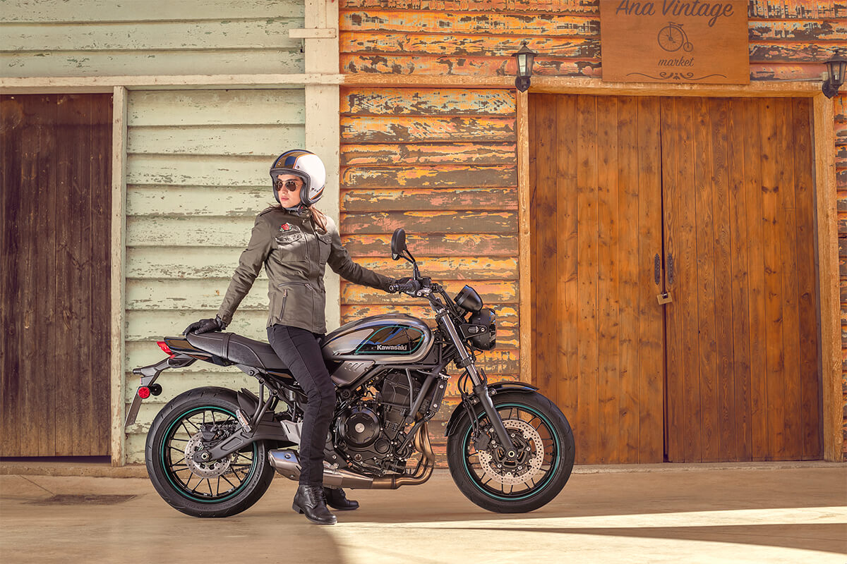 Side angle of a person sitting on a parked motorcycle in front of old buildings.