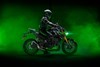 Side angle of a person sitting on a parked motorcycle in front of green smoke.