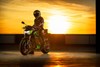 Three-quarter front angle of a person sitting on their parked motorcycle in front of a sunset.