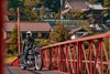 Three-quarter front angle of a person sitting on their motorcycle in the middle of a red bridge.
