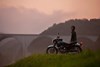 Side angle of a person standing next to their motorcycle on top of a cliff.