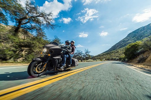Three-quarter front angle of a person riding a motorcycle on a highway with a passenger. opens in a new window