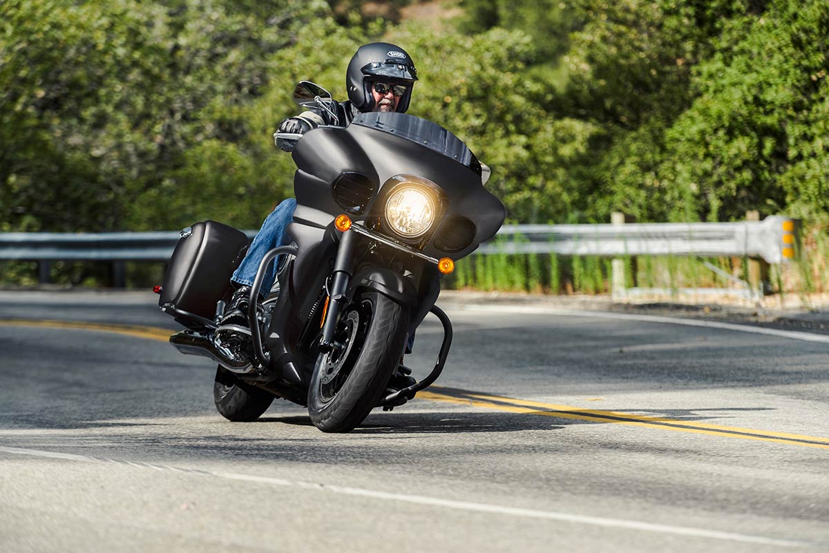 Three-quarter front angle of a person riding a metallic grey motorcycle on a highway.