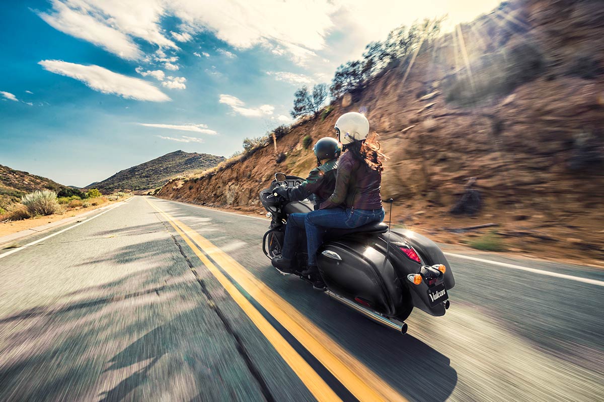 Three-quarter rear angle of a person riding a motorcycle on a highway.
