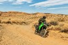 Three-quarter front angle of a person riding a lime green motorcycle over a dirt trail.