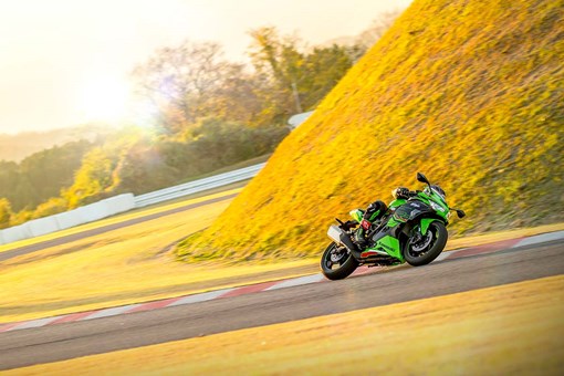 Three-quarter front angle of a person riding a motorcycle on a track with the sunset behind them. opens in a new window