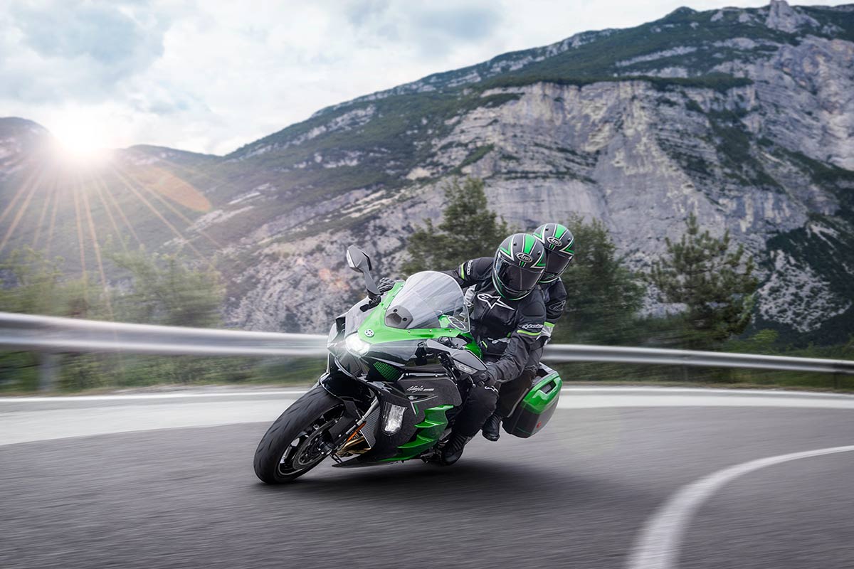 Three-quarter front angle of two people riding on a motorcycle through the mountains.
