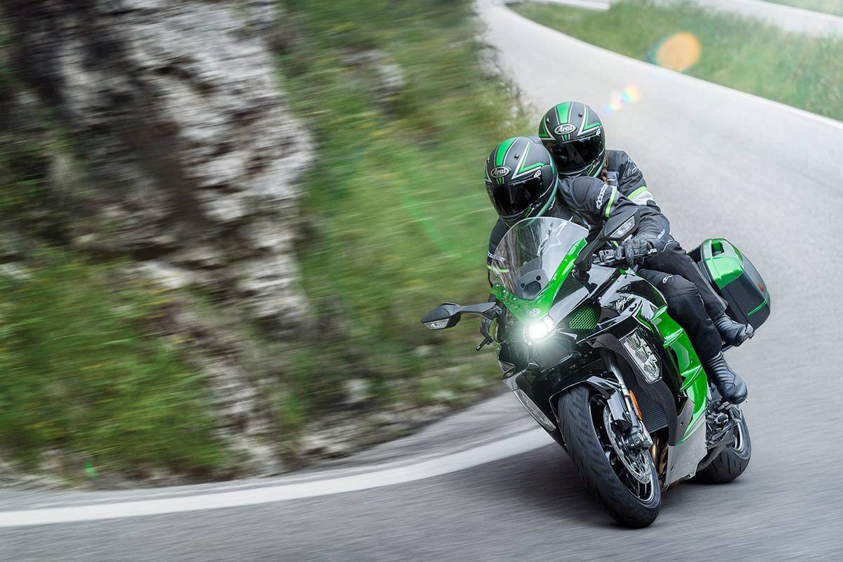 Three-quarter front angle of two people making a turn on a motorcycle on a highway.