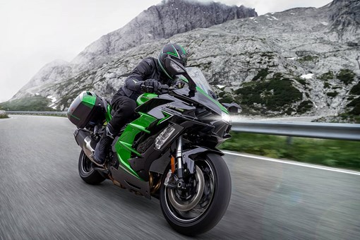 Three-quarter front angle of a person riding a green and black motorcycle on a highway. opens in a new window
