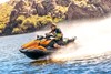 Three-quarter front angle of a person on a personal watercraft on the water with a trail of mist behind them.