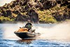 Three-quarter front angle of a person on a personal watercraft on the water with a rocky mountain in the background.